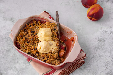 Crumble, Crisp or Cobbler with nectarines, peaches, rolled oats and scoop of ice cream in casserole dish on a metal tray. American cuisine. Easy dessert.