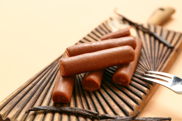 Wooden board with tasty chocolate glazed curd snacks with vanilla flavor on beige background, closeup