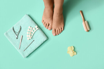 Feet of young woman, flower and set for pedicure on turquoise background