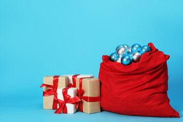 Santa Claus bag with baubles and gift boxes on light blue background, space for text