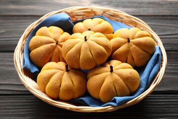 Wicker basket with tasty pumpkin shaped buns on wooden table, closeup