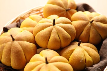 Wicker basket with tasty pumpkin shaped buns on beige background, closeup