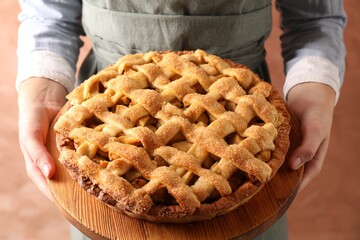 Woman holding wooden board with tasty homemade apple pie on light coral background, closeup