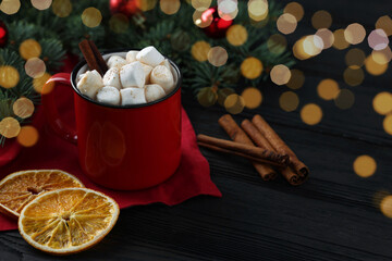 Tasty hot cocoa drink with marshmallows in mug and spices on black wooden table, closeup