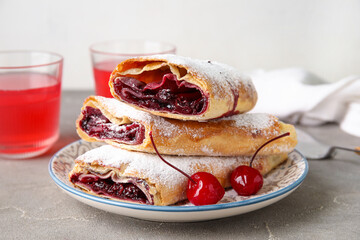 Plate with sweet cherry strudel and glasses of juice on grey table