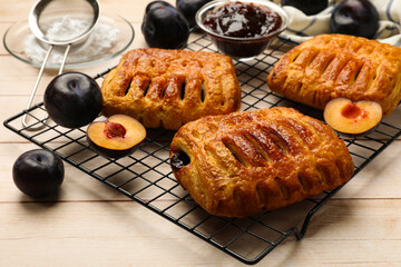 Delicious puff pastries and plums on white wooden table, closeup