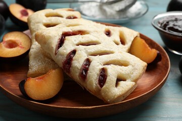 Delicious puff pastries and plums on light blue wooden table, closeup