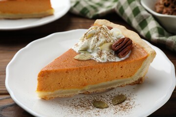 Piece of tasty homemade pumpkin pie with whipped cream, seeds and pecan nut on table, closeup