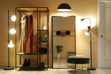 Rack with clothes, mirror and glowing lamps in interior of hallway © Pixel-Shot