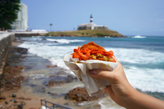 Acaraje in Salvador de Bahia, Brazil. Brazilian traditional dish Acaraje street food from Northeast Brazil with Farol da Barra Lighthouse and Bay of All Saints, Salvador de Bahia, Brazil.