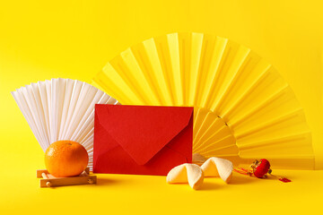 Red envelope with fans, fortune cookies and mandarin on yellow background. New Year celebration