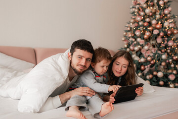 Happy family laughing and having fun together on the bed. Two parents playing with their son in tablet at home. Mom and dad spending quality time with their children on the weekend. Part of a series