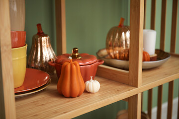 Shelving unit with candles in shape of pumpkin, cups with saucers and decor near green wall. Closeup