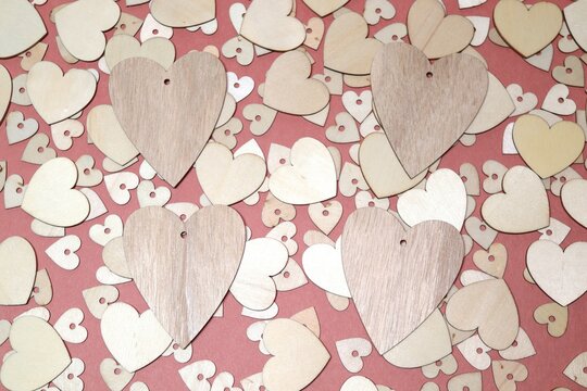 Four wooden hearts on top of a collection of slightly smaller wooden heart on top of a layer of even smaller hearts on a dark pink background
