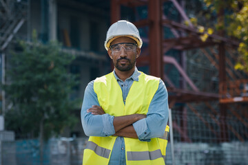 Handsome man with worker's helmet with folded arms standing near a construction