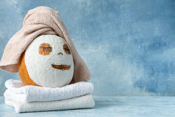 Pumpkin with drawn face, clay mask and towels on blue grunge background