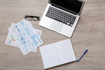Modern laptop with graphics and notebook on brown wooden background