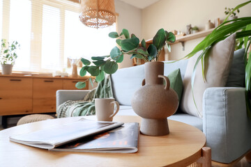 Coffee table with branches in vase, cup and magazines in room. Closeup