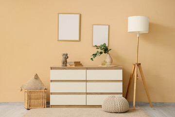 Chest of drawers with floor lamp, basket with pillow and pouf near beige wall
