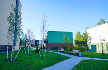 Modern Townhouse along sidewalk with green lawn.Pedestrian path with flowerbed shrubs. Townhouse in a suburb area. New apartment buildings in green enviroment. Street  with Two-story townhouses.