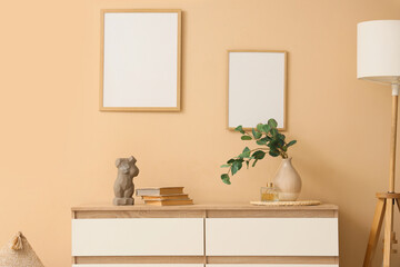 Chest of drawers with branches in vase, books and frames on beige wall in room
