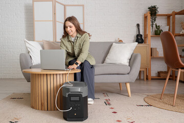 Young woman charging laptop with portable power station at home