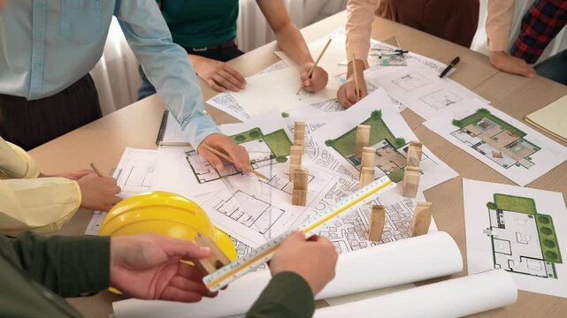 Architect and safety engineer discussion about building construction use blueprint on table with architectural document, measurement tool and wooden block scatter around at modern office. Delineation.