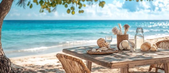 A wooden table with seashells, a glass, and a bottle of water is set on a beach with a view of the ocean.