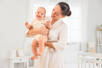 Happy mother holding her little baby in bedroom