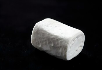 a single marshmallow with a glossy surface, showcasing its fluffy texture, isolated on a dark velvet background, with soft shadows highlighting its contours create with ai