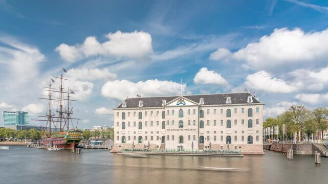 Hyperlapse of the National Maritime Museum with the sailboat replica Amsterdam docked nearby. Blue sky with clouds timelapse. Famous for cultural activity, canals and bridges. Amsterdam, Netherlands
