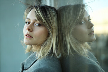 Lovely Caucasian modern girl leaning against the window glass, thinks about problems and important...