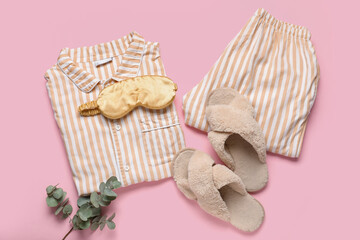 Striped pajamas with sleeping mask, slippers and eucalyptus on pink background