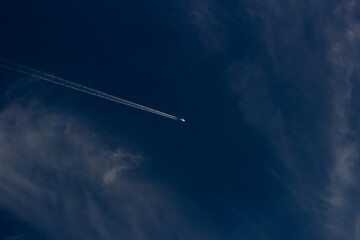 Airplane in the blue sky with white clouds and contrail.
