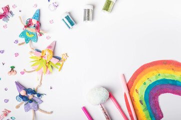 Hand-painted rainbow with fairy dolls and glitter pens for magical creativity. Whimsical fairies and sparkling accessories. Craft supplies featuring fairies with space for notes. Flat lay. Top view.