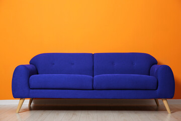 Comfortable blue sofa near orange wall in room