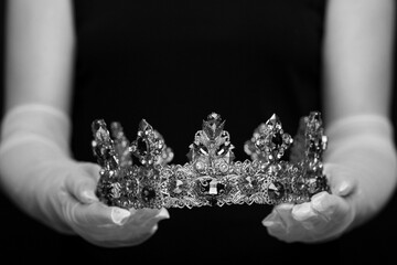 Woman holding luxury crown, closeup. Black-and-white photo