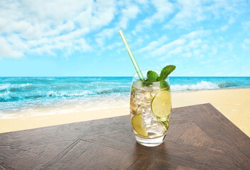 Refreshing drink with straw on wooden table at beach