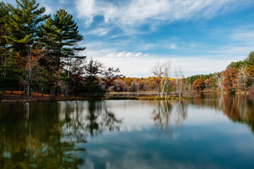 The overhead mid-morning October sky and autumn shoreline reflect off Allen Lake within Hartman Creek State Park, Waupaca, Wisconsin,  the morning sun casts a small ray of light into the picnic area.