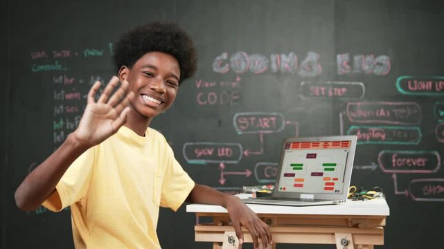 Smart african boy use laptop to code program and turn around to wave hand. Cute high school stident coding engineering prompt or program system at blackboard in STEM technology classroom. Edification