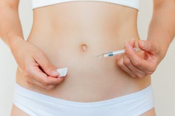 A young Caucasian woman in beige underwear giving herself a subcutaneous injection into her stomach. Women's reproductive health. Ovulation trigger