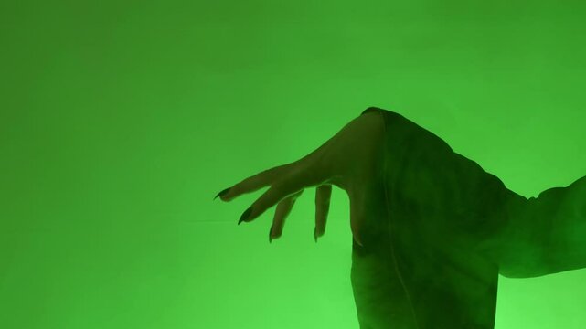 A witch's hand with long, sharp black nails reaches forward, creating a haunting silhouette against a green background. Perfect for spooky Halloween themes