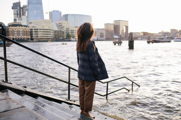 Beautiful young woman stands on steps flooded with water during high tide on the Thames in London