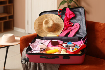 Suitcase with open first aid kit, stylish clothes and passport on sofa in room