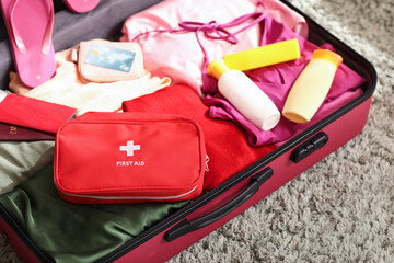 Suitcases with first aid kit, stylish clothes and bottles of sunscreen cream in room