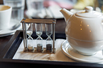 Elegant tea time setup with ceramic teapot and hourglass timer on tray