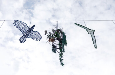 Wire bird sculptures and hanging plants against a cloudy sky