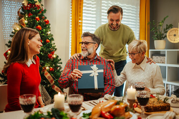 Happy family giving christmas present to senior father during lunch