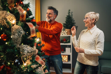 Happy senior couple decorating christmas tree at home