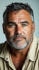 Obraz premium Man with gray hair and beard, wearing a beige shirt, looking directly at the camera